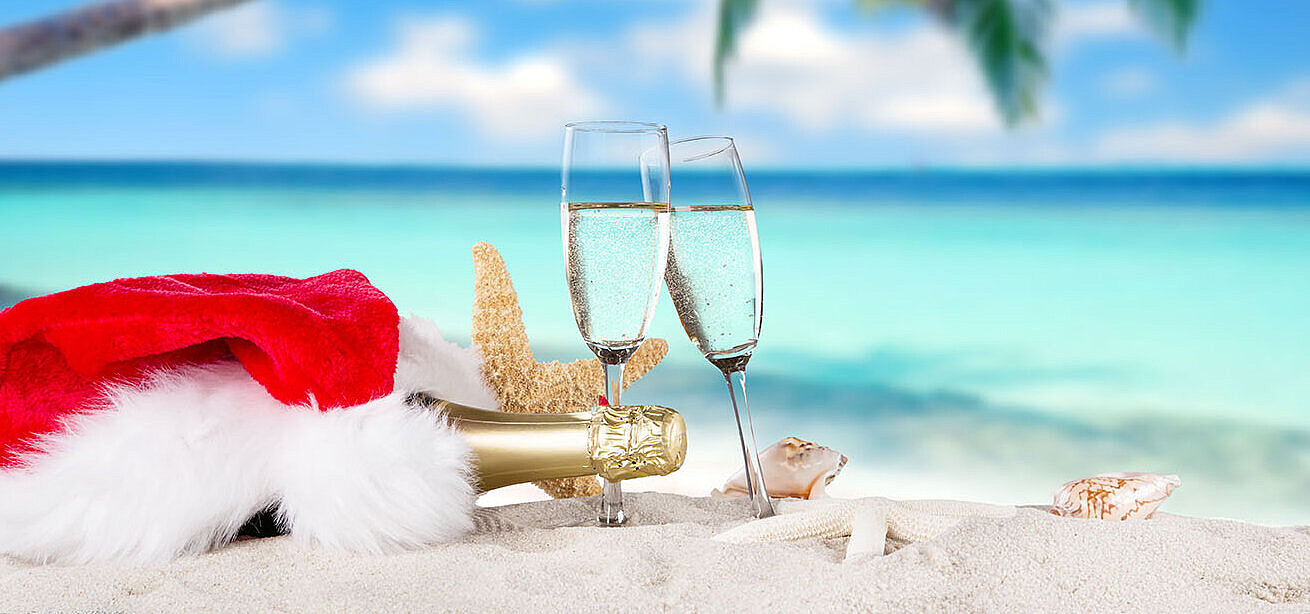 © Lukas Gojda - AdobeStock.com Weihnachten am Strand mit Champagner und Santa-Mütze